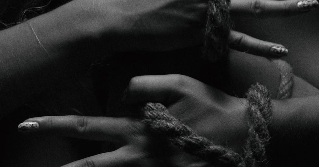 Close-up black and white image of hands tied with a rope, showcasing artistic detail.