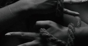Close-up black and white image of hands tied with a rope, showcasing artistic detail.