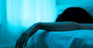 A serene and moody bedroom scene showcasing a person resting with an arm draped over the bed.