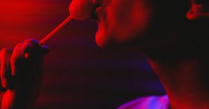 Dramatic portrait of a woman savoring a lollipop under moody red lighting.